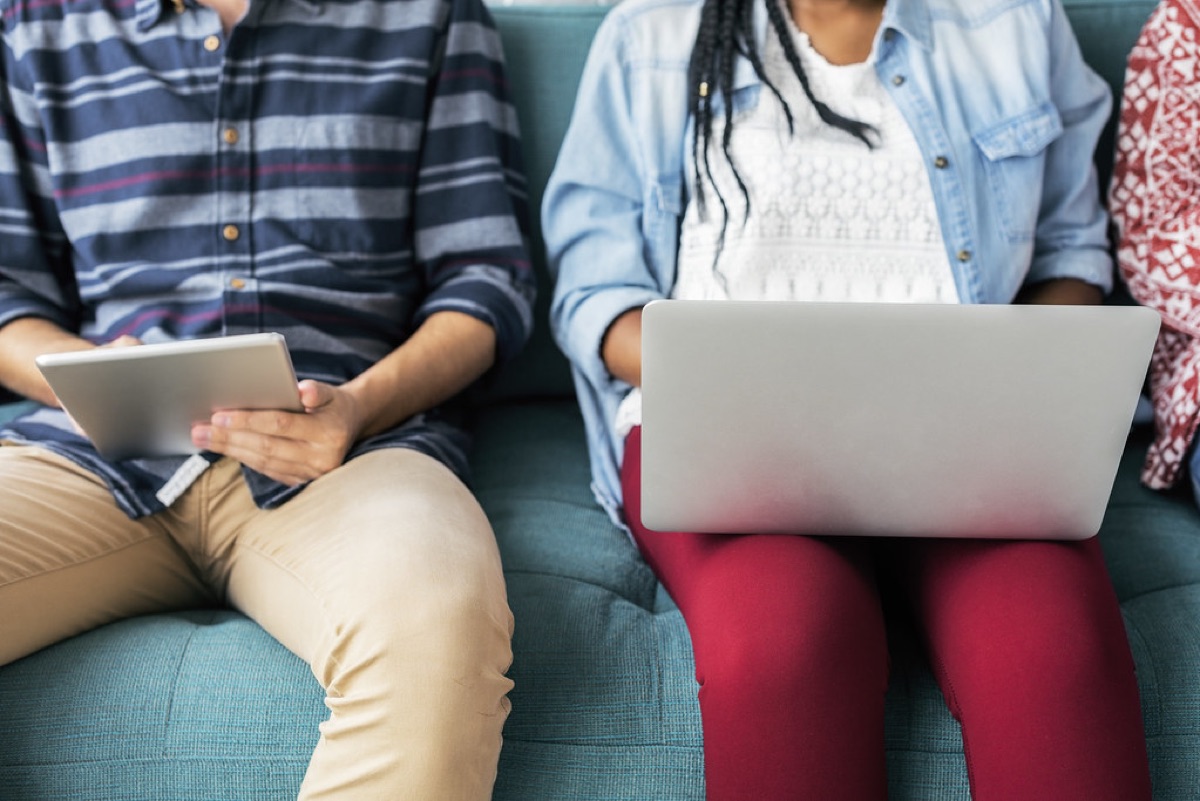 Two people on a teal couch using a laptop